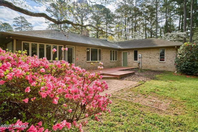 rear view of property featuring brick siding, a yard, a wooden deck, and a chimney