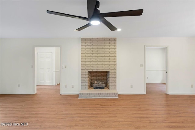 unfurnished living room featuring ceiling fan, light wood finished floors, baseboards, and a fireplace