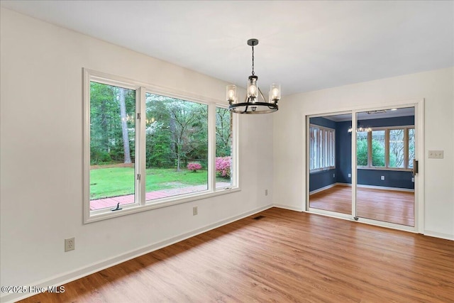 spare room featuring a chandelier, wood finished floors, and baseboards