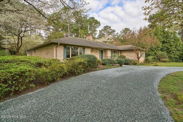 ranch-style house featuring gravel driveway, brick siding, and a chimney