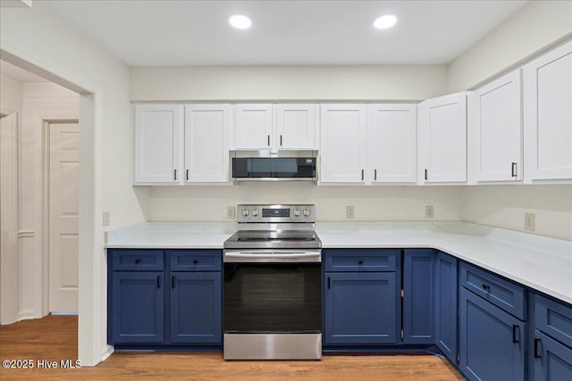 kitchen with appliances with stainless steel finishes, blue cabinetry, white cabinets, light countertops, and light wood-style floors
