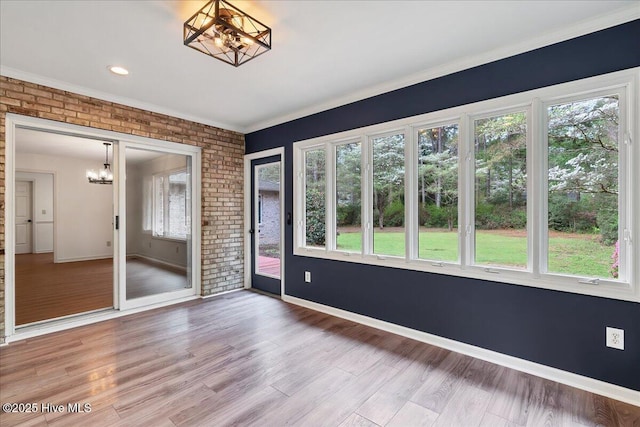spare room featuring a chandelier, healthy amount of natural light, wood finished floors, baseboards, and brick wall