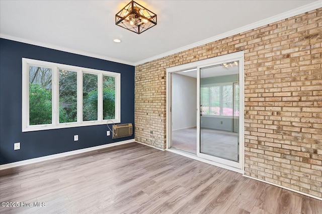 unfurnished room featuring wood finished floors, a wall unit AC, baseboards, brick wall, and crown molding