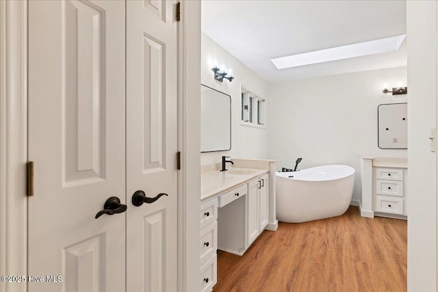full bathroom with a skylight, vanity, a soaking tub, and wood finished floors