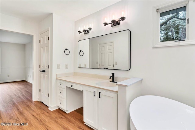 bathroom with wood finished floors, vanity, a freestanding tub, and baseboards