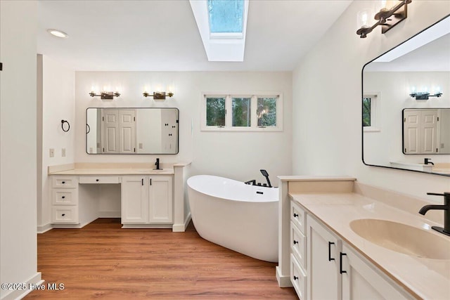 bathroom with a skylight, a freestanding bath, wood finished floors, and two vanities