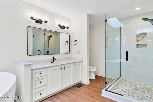 bathroom with a stall shower, vanity, wood finished floors, and toilet