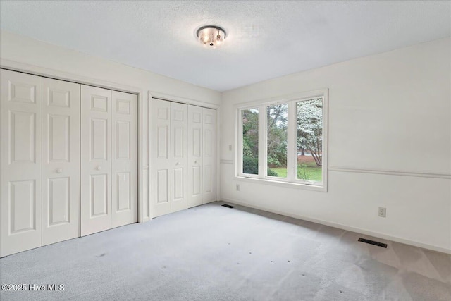 unfurnished bedroom featuring two closets, carpet flooring, a textured ceiling, and baseboards