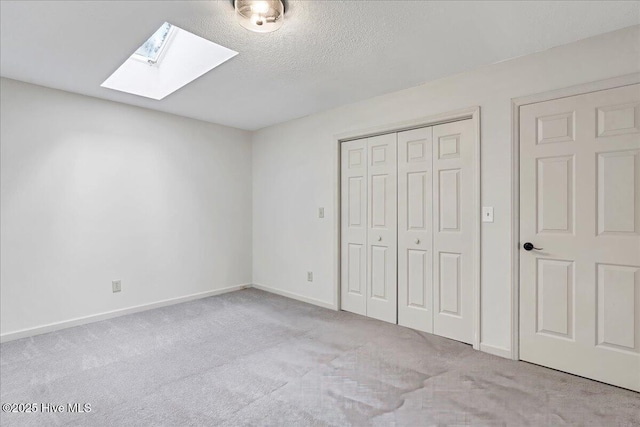 unfurnished bedroom with a skylight, carpet floors, a closet, baseboards, and a textured ceiling