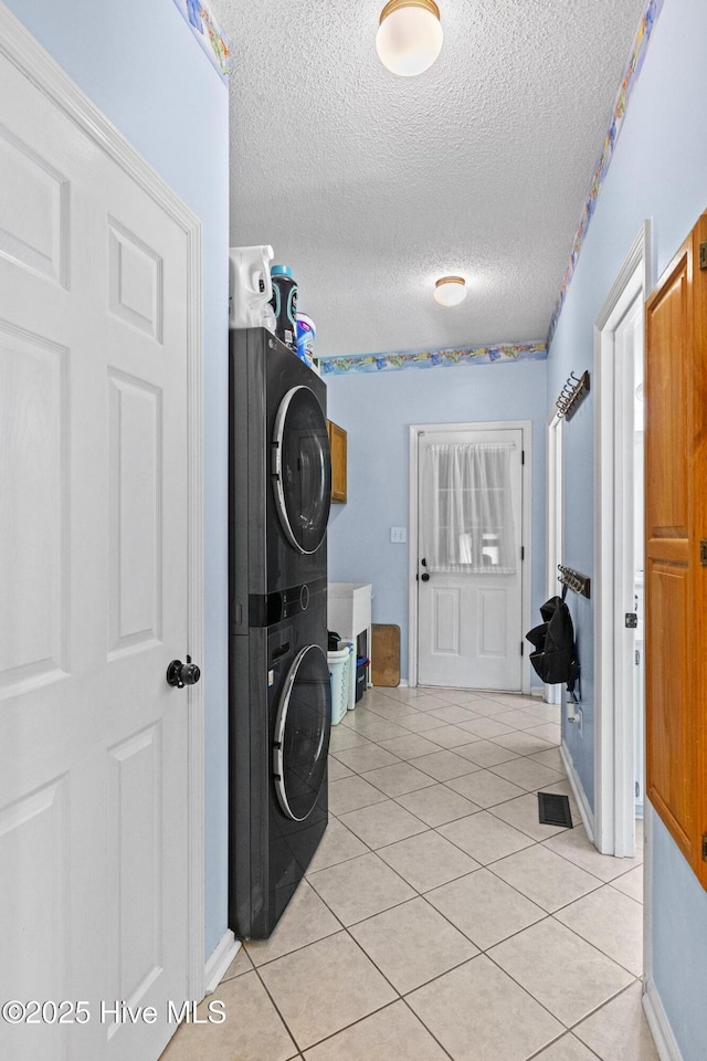 laundry room featuring estacked washer and dryer, a textured ceiling, light tile patterned flooring, cabinet space, and baseboards