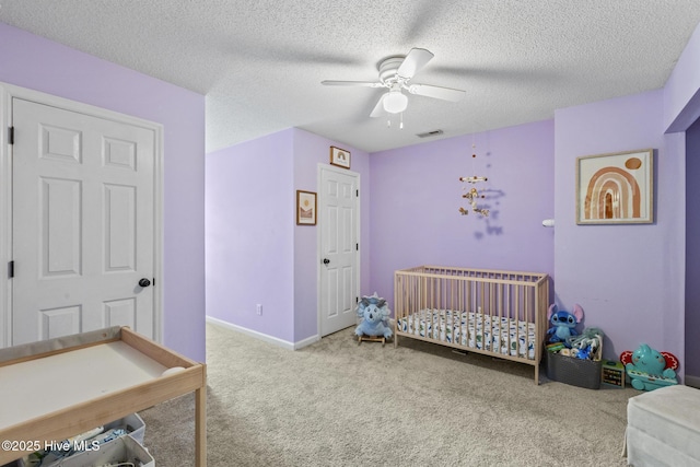 carpeted bedroom featuring a crib, ceiling fan, a textured ceiling, and baseboards