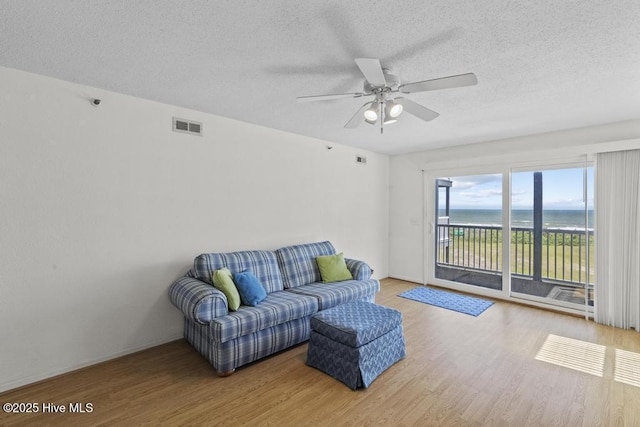 living room with wood finished floors, a textured ceiling, a ceiling fan, and a water view