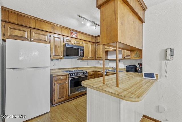 kitchen with freestanding refrigerator, black microwave, range with electric stovetop, a peninsula, and light wood-type flooring