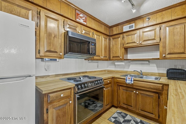 kitchen with freestanding refrigerator, range with electric cooktop, black microwave, a sink, and wooden counters