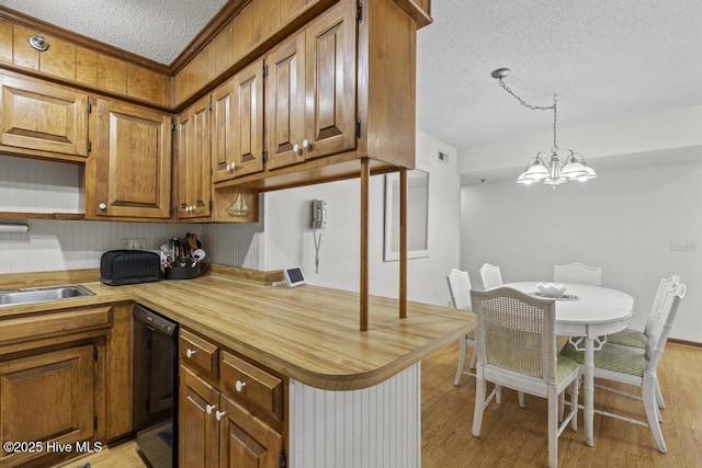 kitchen featuring a textured ceiling, dishwasher, a chandelier, light wood-style floors, and brown cabinetry