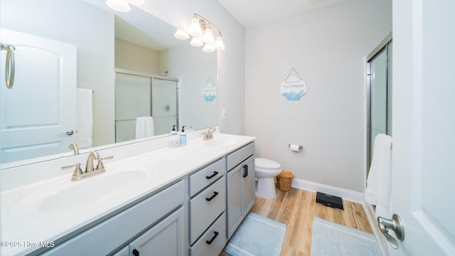full bath with a shower stall, wood finished floors, baseboards, double vanity, and toilet