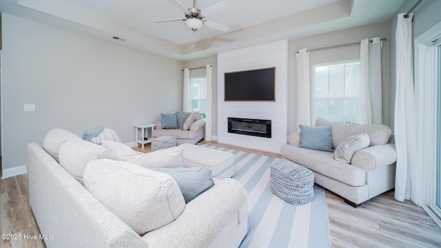 living area featuring plenty of natural light, ceiling fan, and a raised ceiling