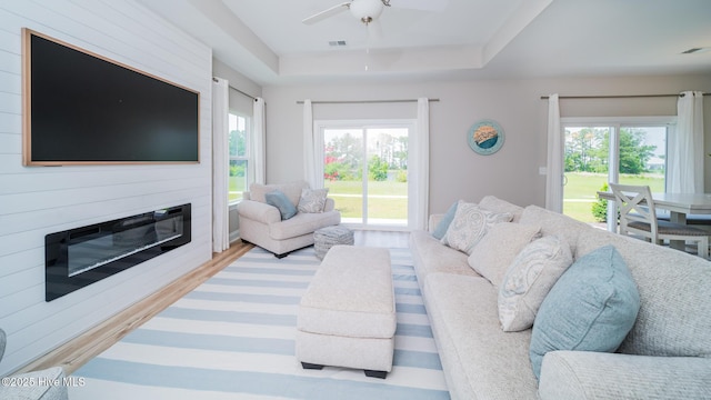 living room with a raised ceiling, a fireplace, a ceiling fan, and wood finished floors