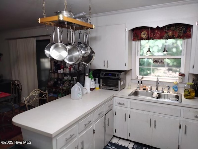 kitchen featuring a sink, light countertops, white cabinetry, crown molding, and a peninsula