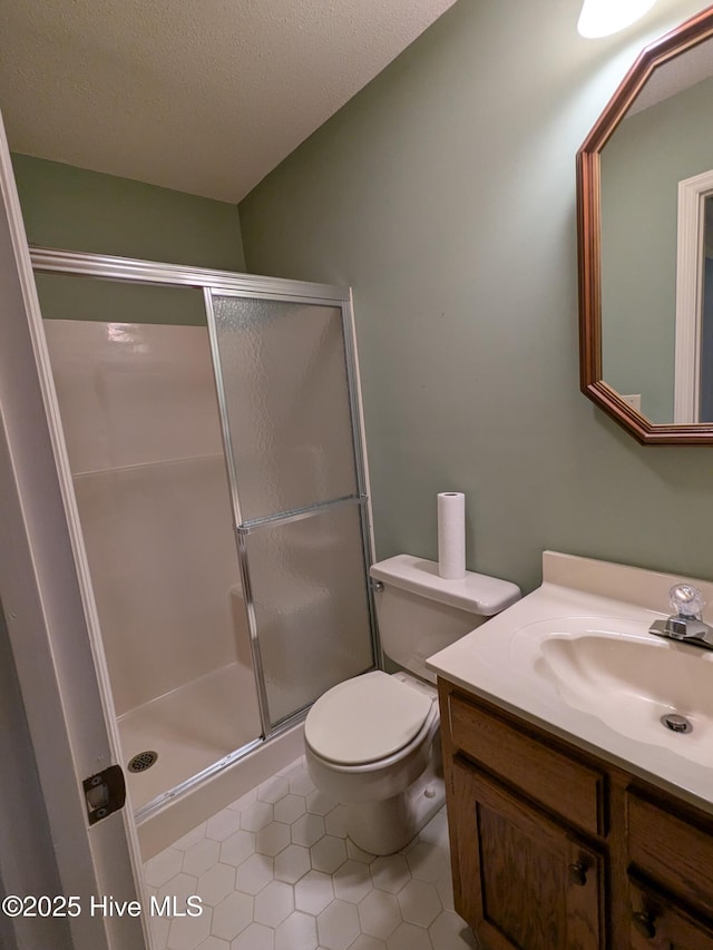 bathroom featuring tile patterned flooring, a shower stall, vanity, and toilet