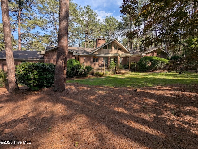 view of front facade with brick siding, a front yard, and a chimney
