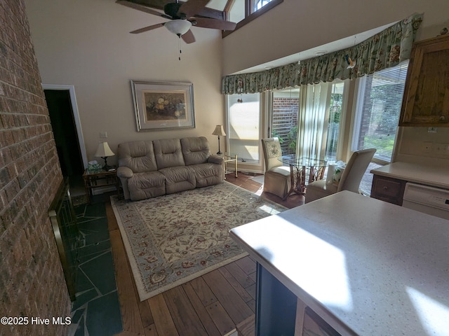 living area with a ceiling fan, hardwood / wood-style flooring, plenty of natural light, and a towering ceiling