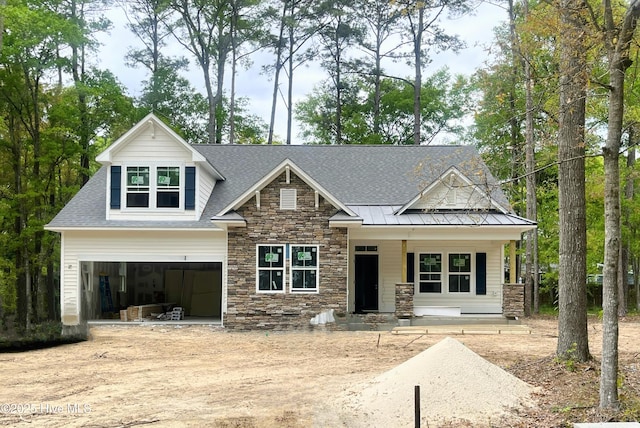 view of front facade with stone siding, dirt driveway, an attached garage, covered porch, and a standing seam roof