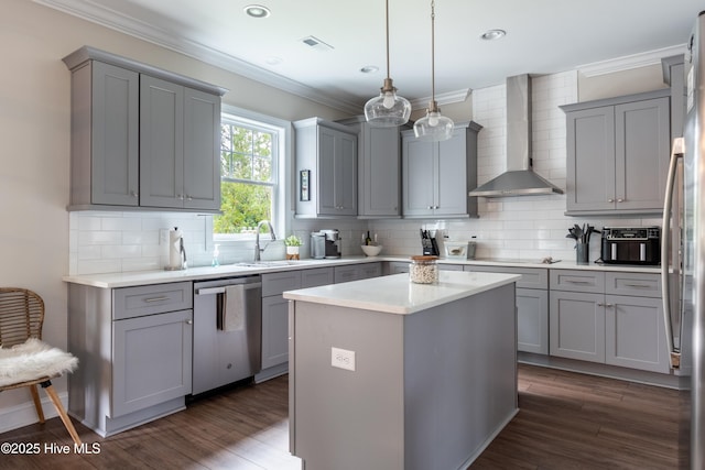 kitchen with appliances with stainless steel finishes, gray cabinetry, wall chimney range hood, a sink, and crown molding