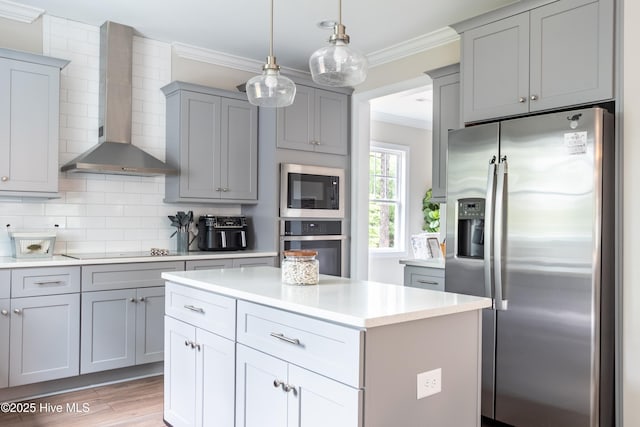 kitchen with appliances with stainless steel finishes, wall chimney range hood, gray cabinetry, and crown molding