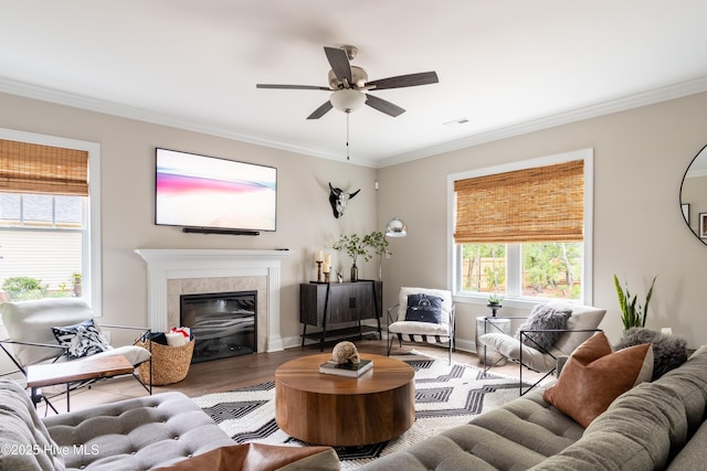 living area with crown molding, wood finished floors, a ceiling fan, a tile fireplace, and baseboards