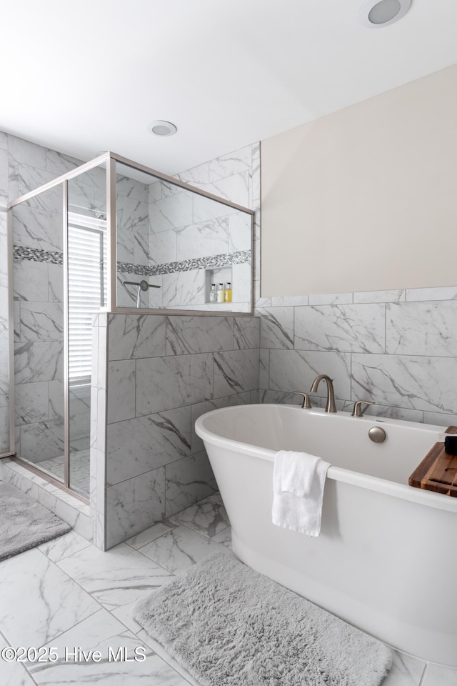bathroom featuring a marble finish shower, marble look tile flooring, a freestanding bath, and tile walls