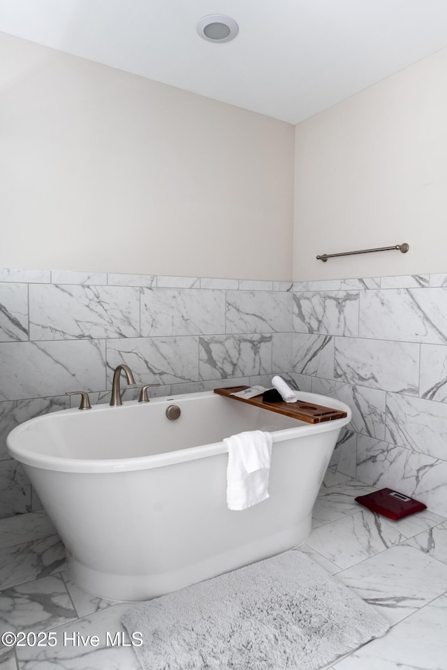 full bathroom featuring marble look tiles, tile walls, a freestanding bath, and wainscoting
