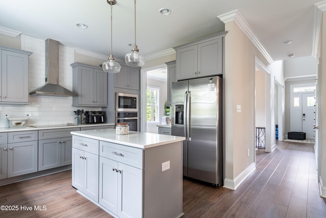 kitchen featuring stainless steel appliances, wall chimney range hood, gray cabinets, a center island, and decorative backsplash
