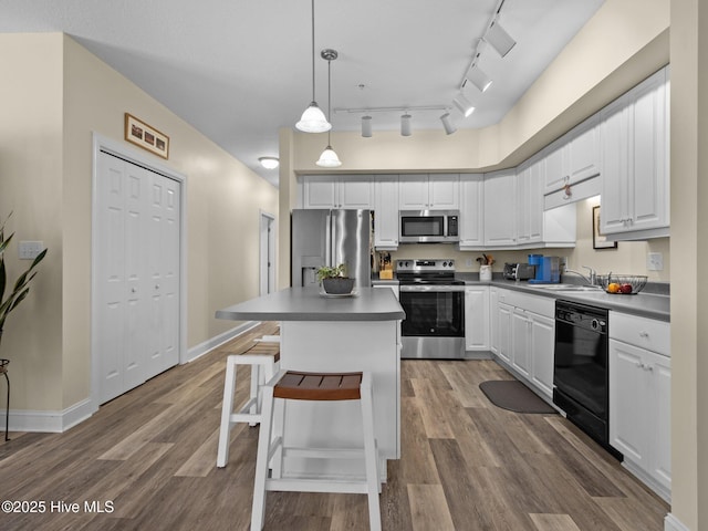 kitchen with stainless steel appliances, a sink, dark wood finished floors, white cabinets, and decorative light fixtures