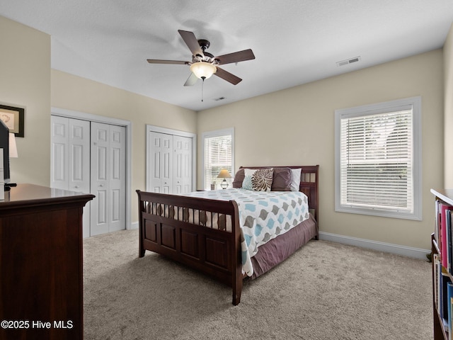 bedroom featuring two closets, light carpet, multiple windows, and baseboards