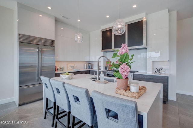 1326 Tidalwalk Dr, Wilmington, NC 28409 - kitchen with stainless steel built in fridge, modern cabinets, a kitchen island with sink, baseboards, and hanging light fixtures