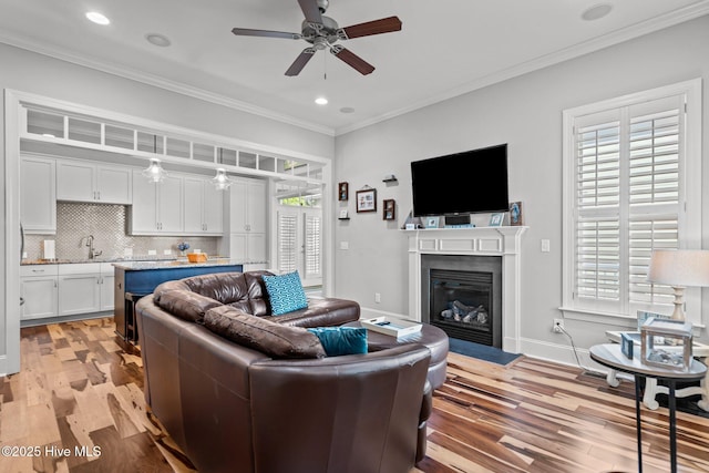 1218 Pinfish Ln, Carolina Beach, NC 28428 - living room featuring a ceiling fan, ornamental molding, light wood-style floors, a fireplace with flush hearth, and recessed lighting