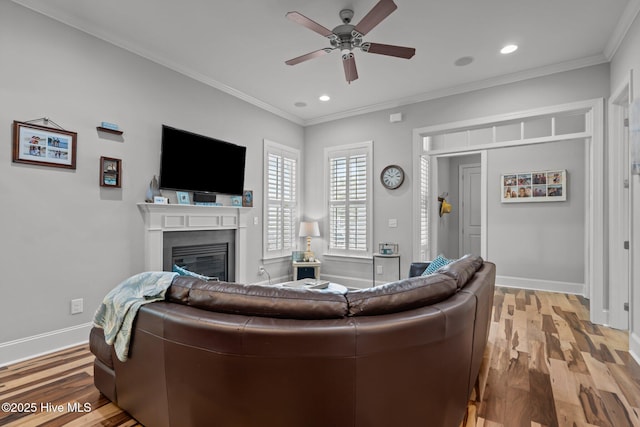 1218 Pinfish Ln, Carolina Beach, NC 28428 - living room featuring a ceiling fan, light wood-type flooring, a glass covered fireplace, baseboards, and ornamental molding