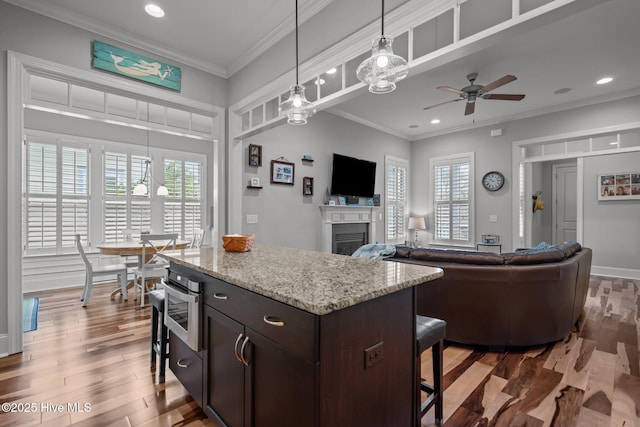 1218 Pinfish Ln, Carolina Beach, NC 28428 - kitchen featuring ceiling fan, stainless steel oven, a glass covered fireplace, a breakfast bar, and wood finished floors