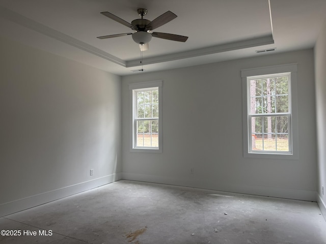 empty room with a raised ceiling, baseboards, ceiling fan, and concrete floors