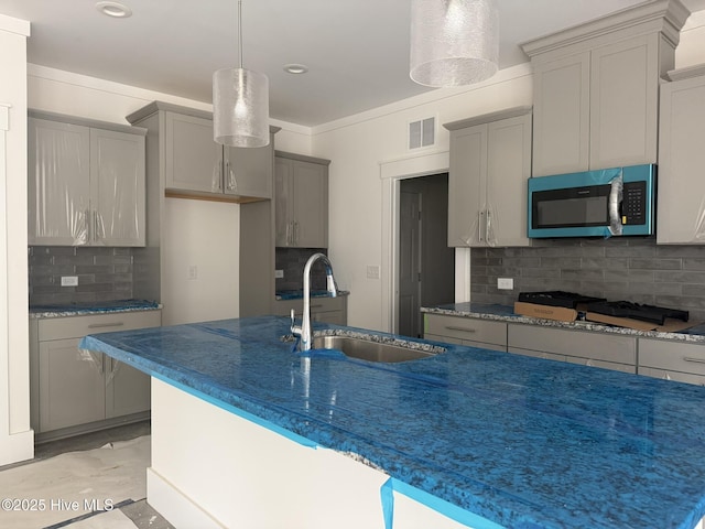 kitchen with stainless steel microwave, a sink, decorative backsplash, gray cabinetry, and gas stovetop