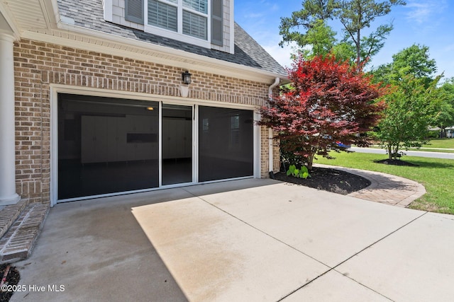 view of exterior entry with brick siding, driveway, a shingled roof, and a garage