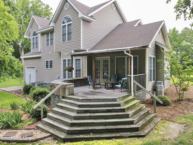 rear view of house featuring french doors, a deck, a shingled roof, and a garage