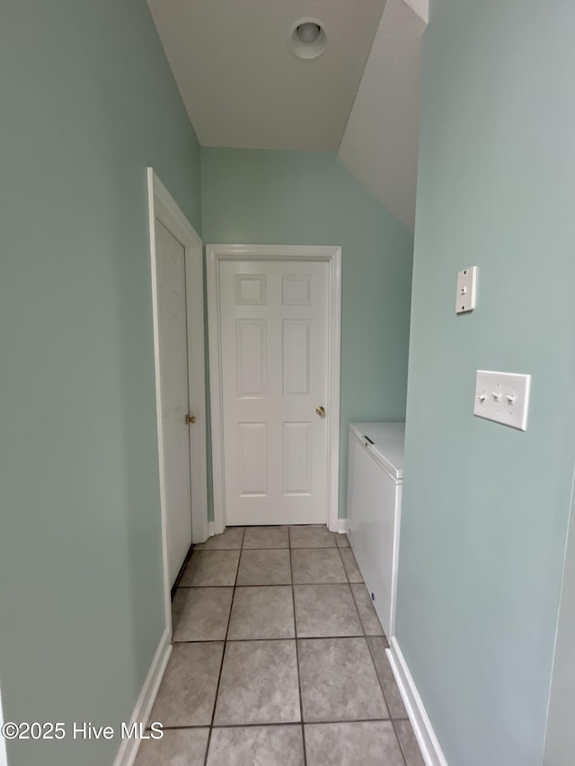 hallway with washer / clothes dryer, light tile patterned floors, and baseboards