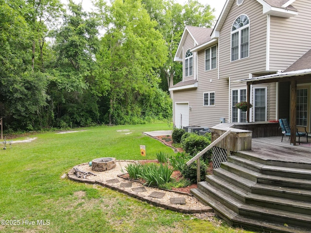 view of grassy yard with a fire pit, a deck, an attached garage, and central AC