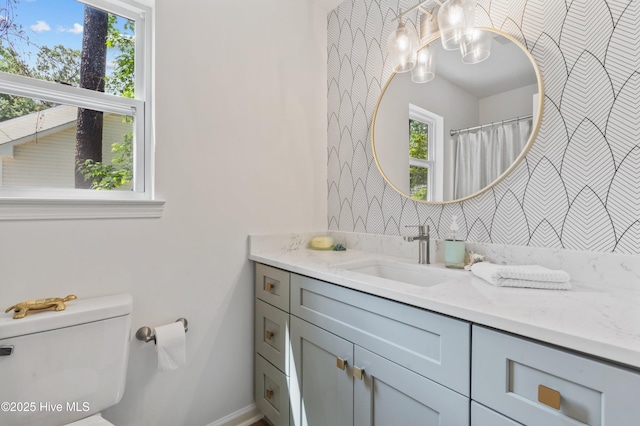 bathroom with wallpapered walls, a chandelier, toilet, vanity, and baseboards