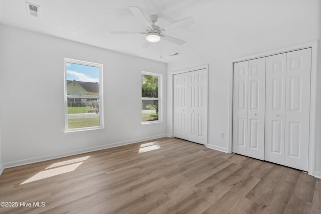 unfurnished bedroom with light wood-type flooring, two closets, baseboards, and ceiling fan