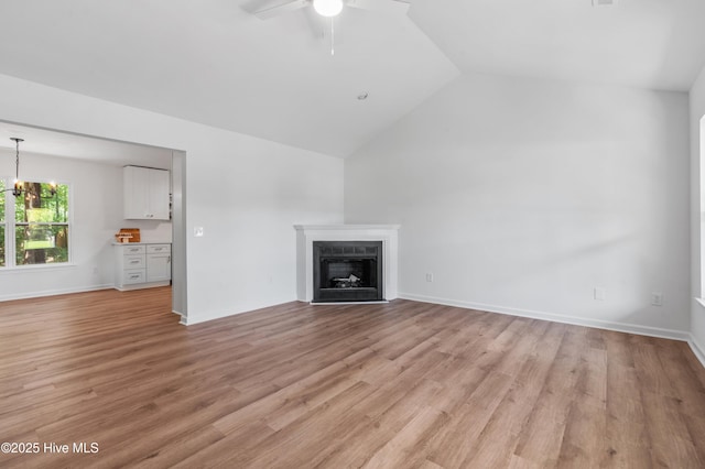 unfurnished living room with vaulted ceiling, a fireplace, ceiling fan, light wood-style floors, and baseboards