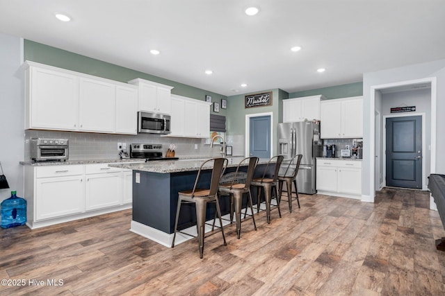 kitchen featuring stainless steel appliances, backsplash, a kitchen breakfast bar, an island with sink, and light wood-style flooring