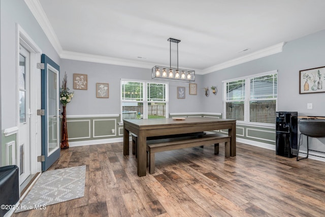 dining space featuring healthy amount of natural light, crown molding, wood finished floors, a decorative wall, and a wainscoted wall